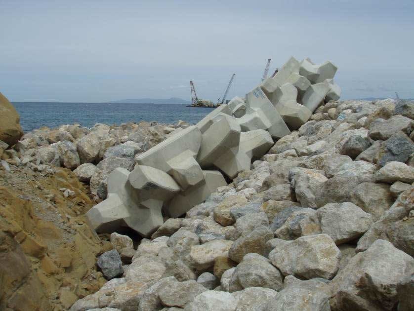 Accropodi in calcestruzzo armato posati su scogliera rocciosa con gru navale sullo sfondo